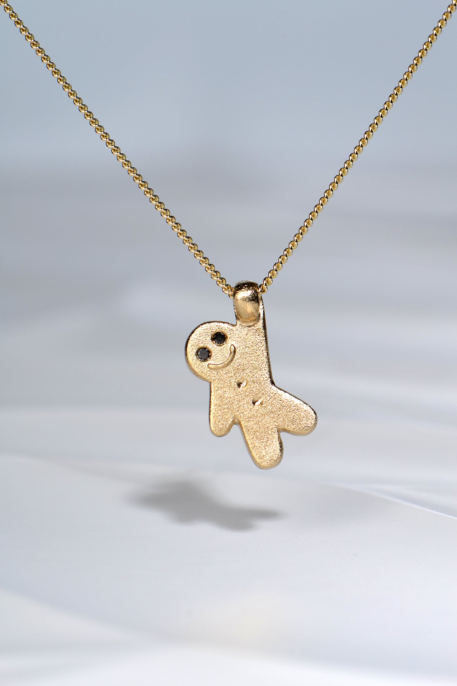 cute gold necklace in the shape of a gingerbread man with two black diamond eyes from jewellery designer Christine Sadler