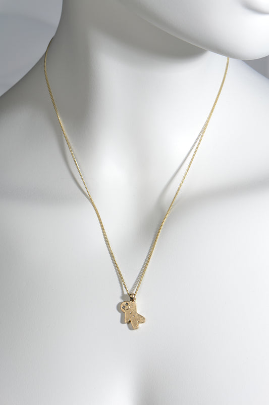 adorable delicate gold necklace in the shape of a tiny gingerbread man with black diamond eyes hanging from a gold curb chain. Designer Christine Sadler