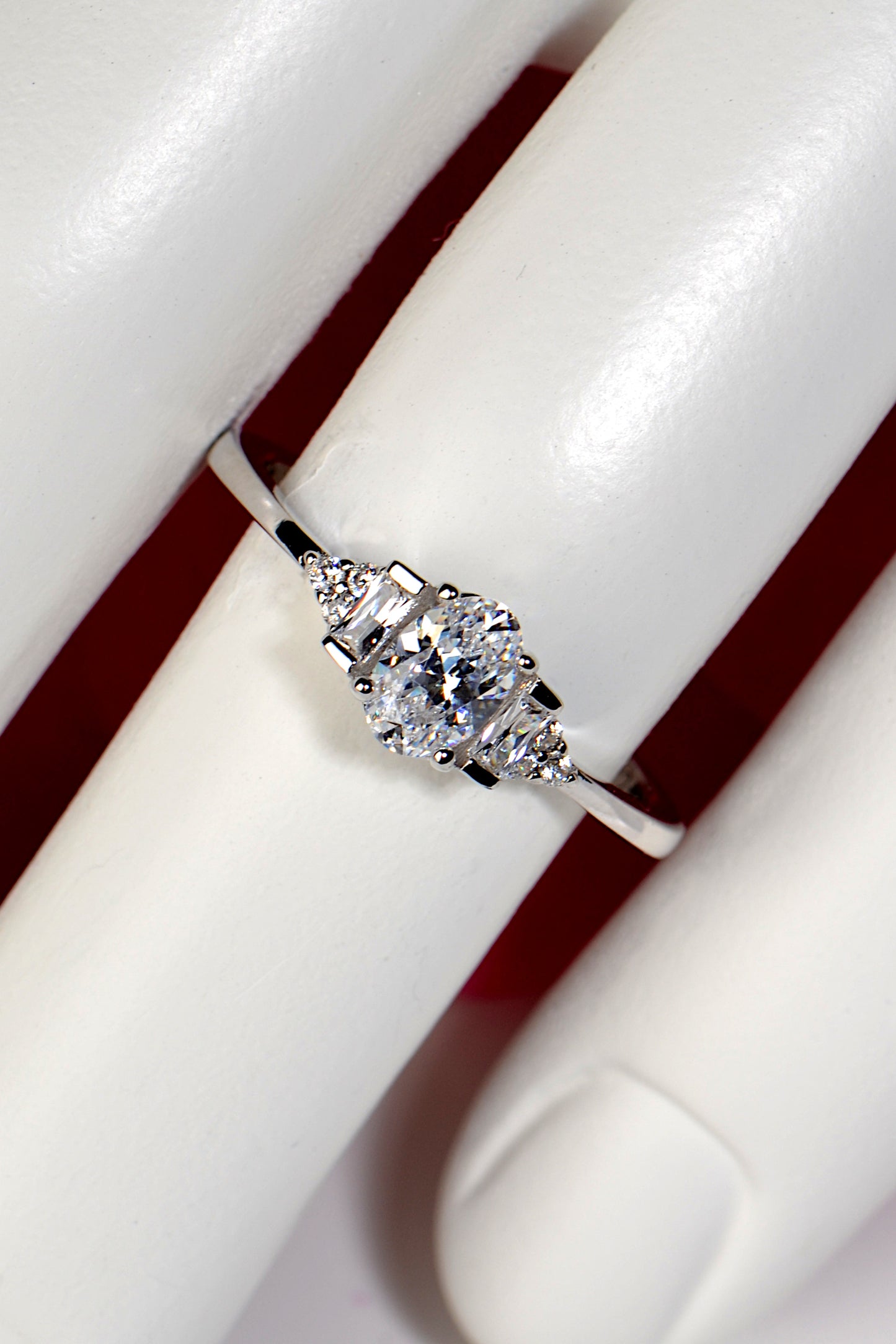 modern delicate platinum oval cut engagement ring with baguette diamonds and rounds as diamond accents shown on a finger