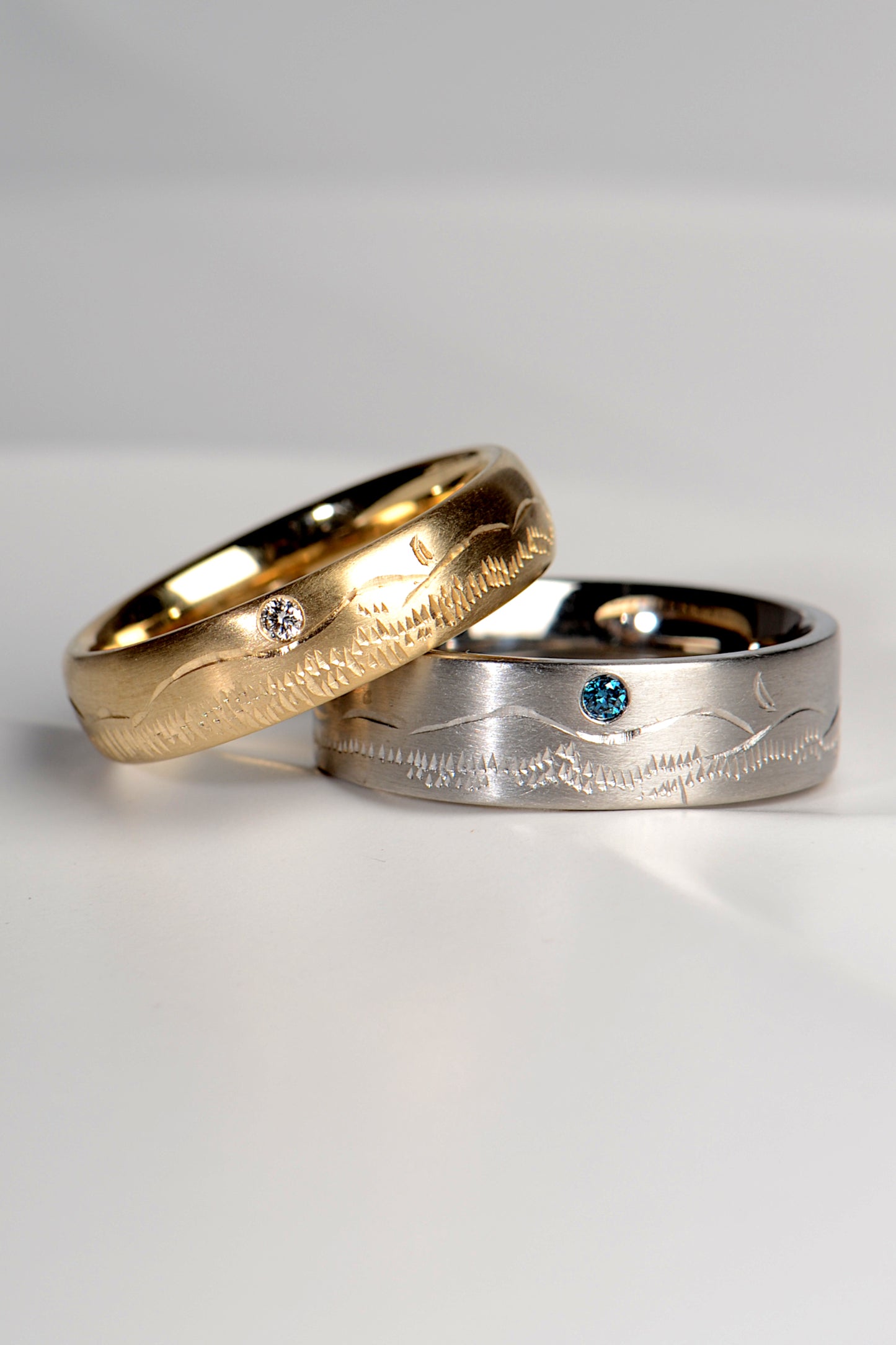 gold and platinum matching his and hers wedding rings set with blue and white diamonds with a mountain pattern hand engraved from jewellery designer Christine Sadler