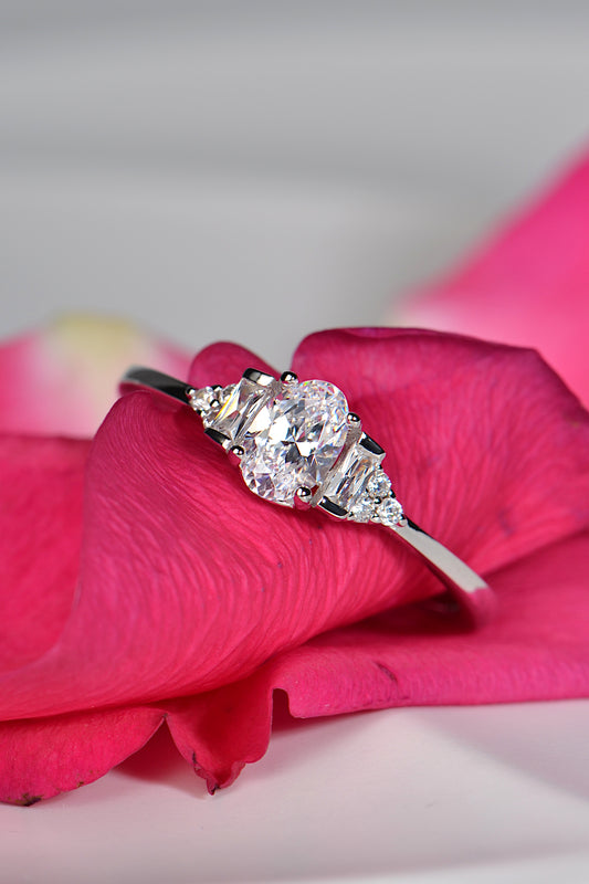 delicate oval cut platinum engagement ring with baguette diamonds and rounds in the shoulders on deep pink rose petals